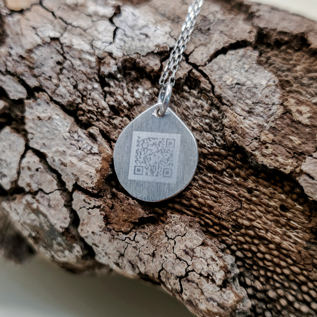 Őrzött Hang kör alakú ezüst medál hátoldala, gravírozott QR-kóddal, amelyen keresztül a személyes hangüzenet újra meghallgatható.