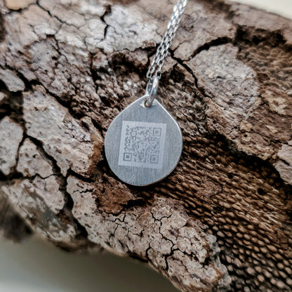 Őrzött Hang kör alakú ezüst medál hátoldala, gravírozott QR-kóddal, amelyen keresztül a személyes hangüzenet újra meghallgatható.